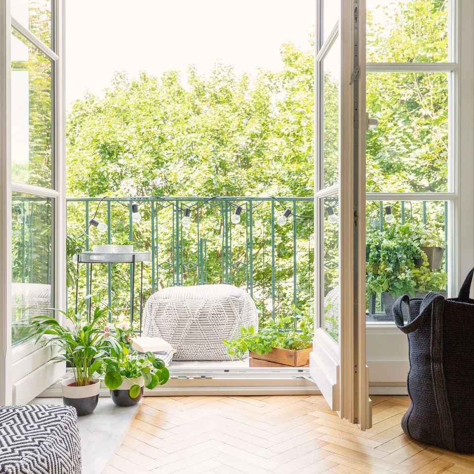 Open white glazed doors leading from a bright room to a planted balcony
